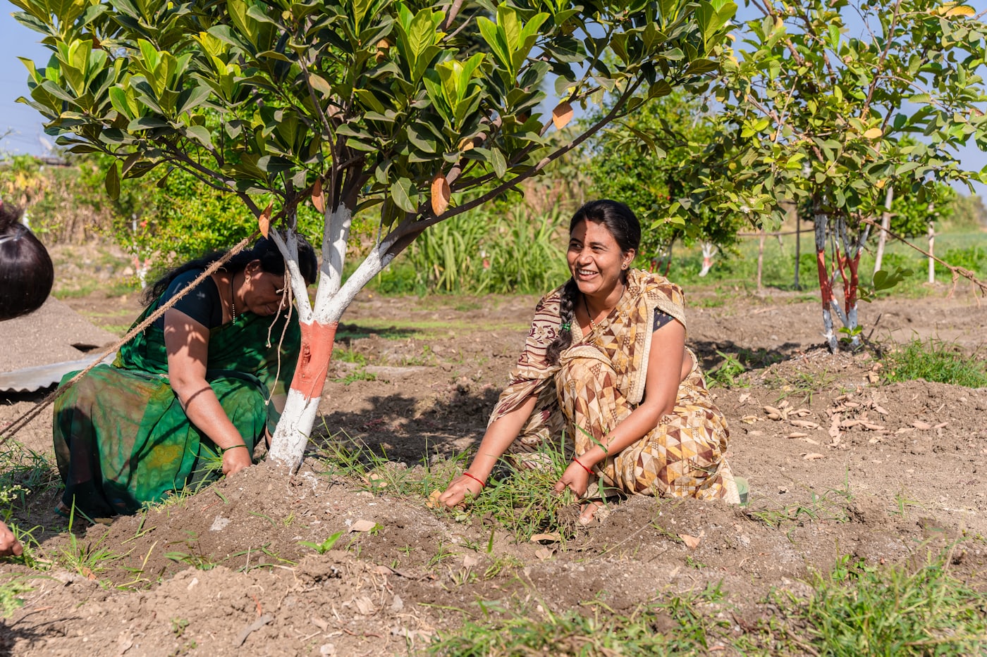 Two women smiling beside a young tree they are tending